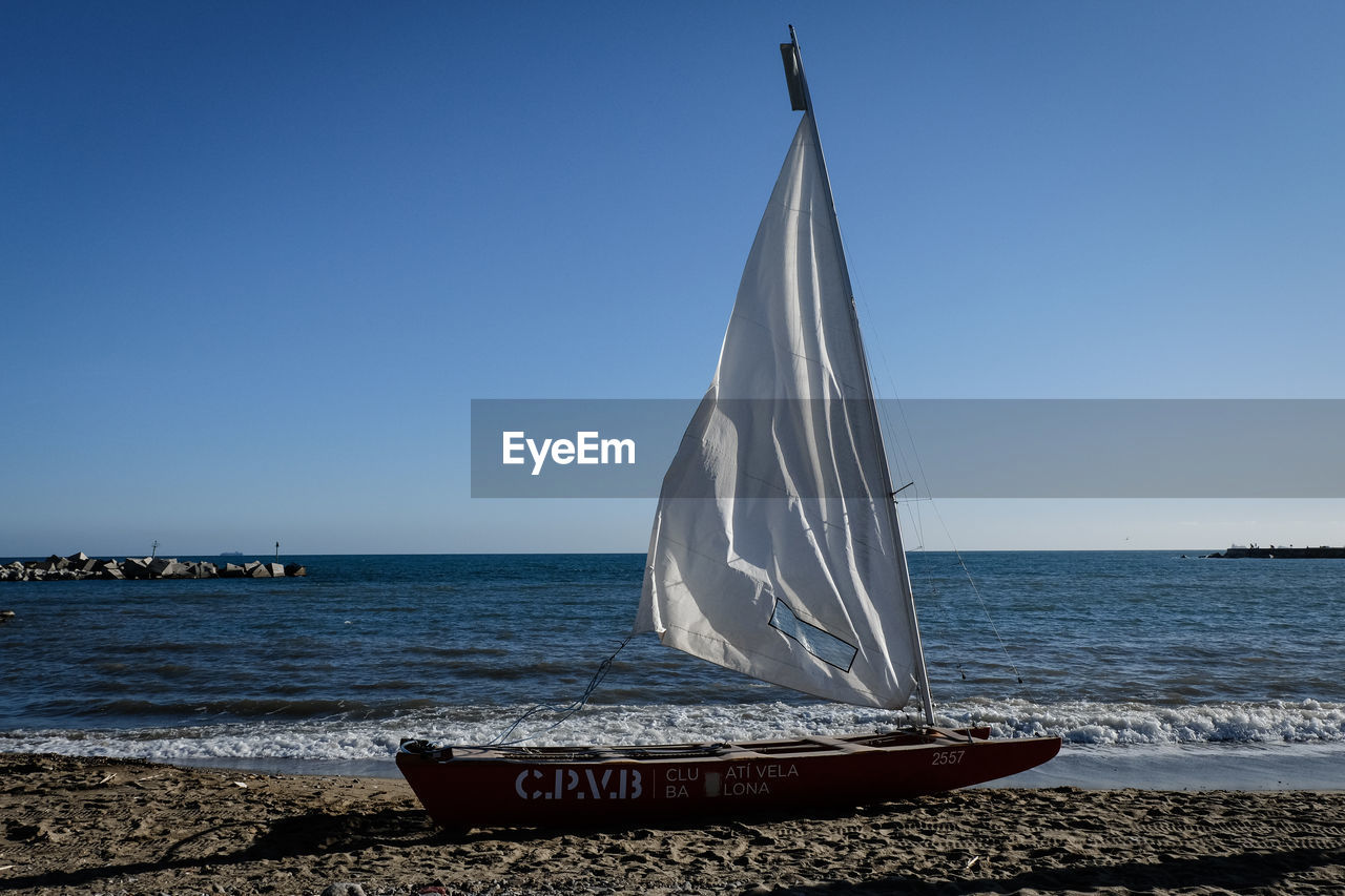 SAILBOAT ON SEA SHORE AGAINST CLEAR SKY