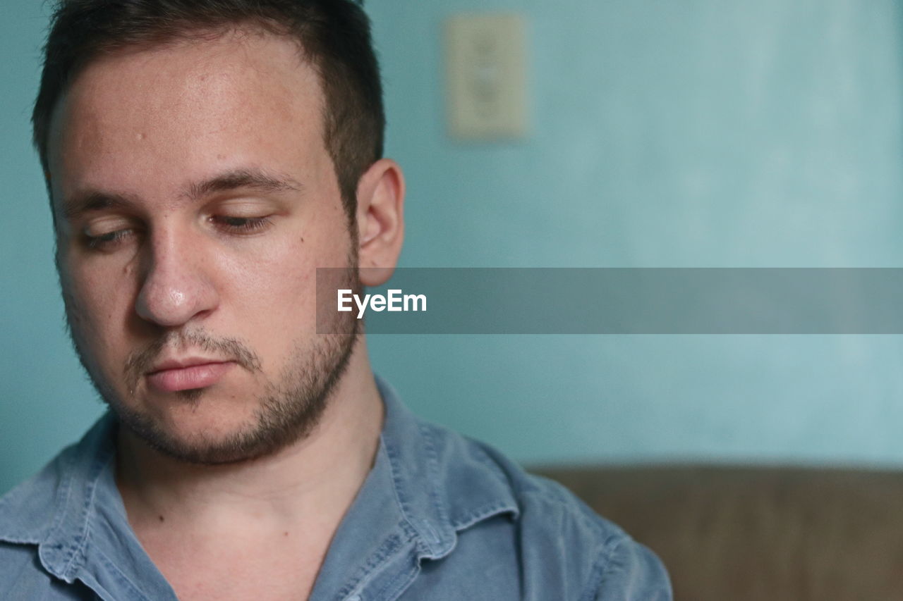 CLOSE-UP PORTRAIT OF YOUNG MAN LOOKING AWAY AGAINST WALL