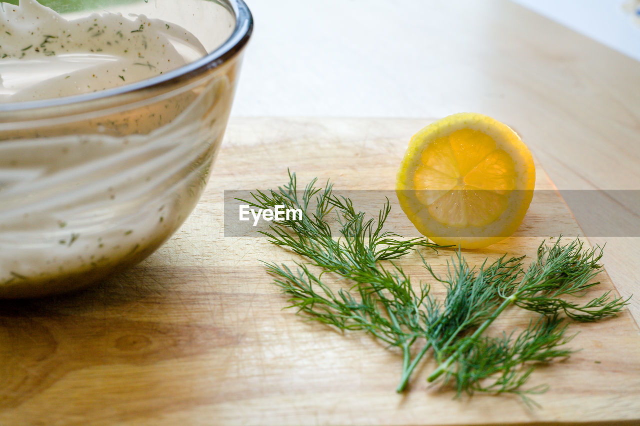 High angle view of mayonnaise in bowl by lemon slice and rosemary on cutting board