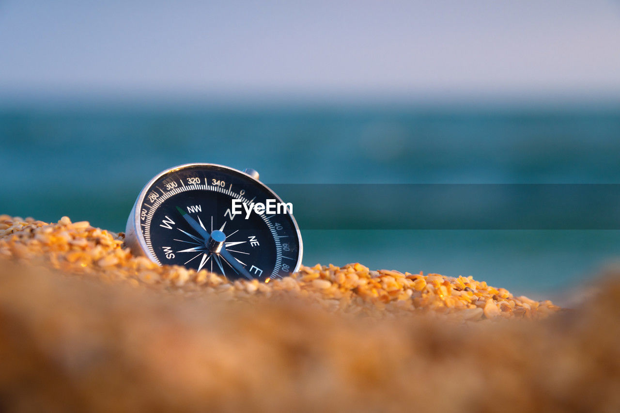 Conceptual photo of a compass in coarse sand against the background of the sea and sky, close-up