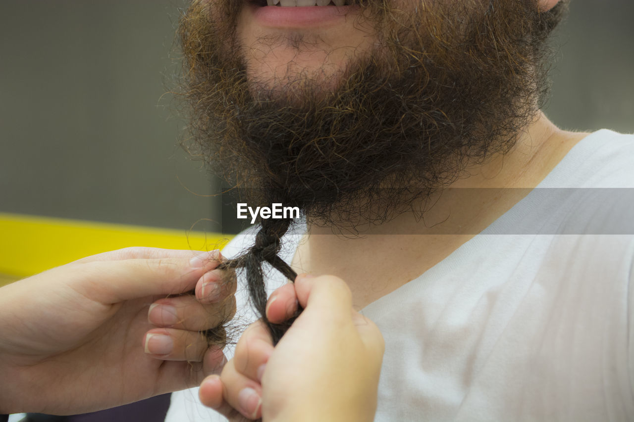 Cropped hands of person tying beard of man