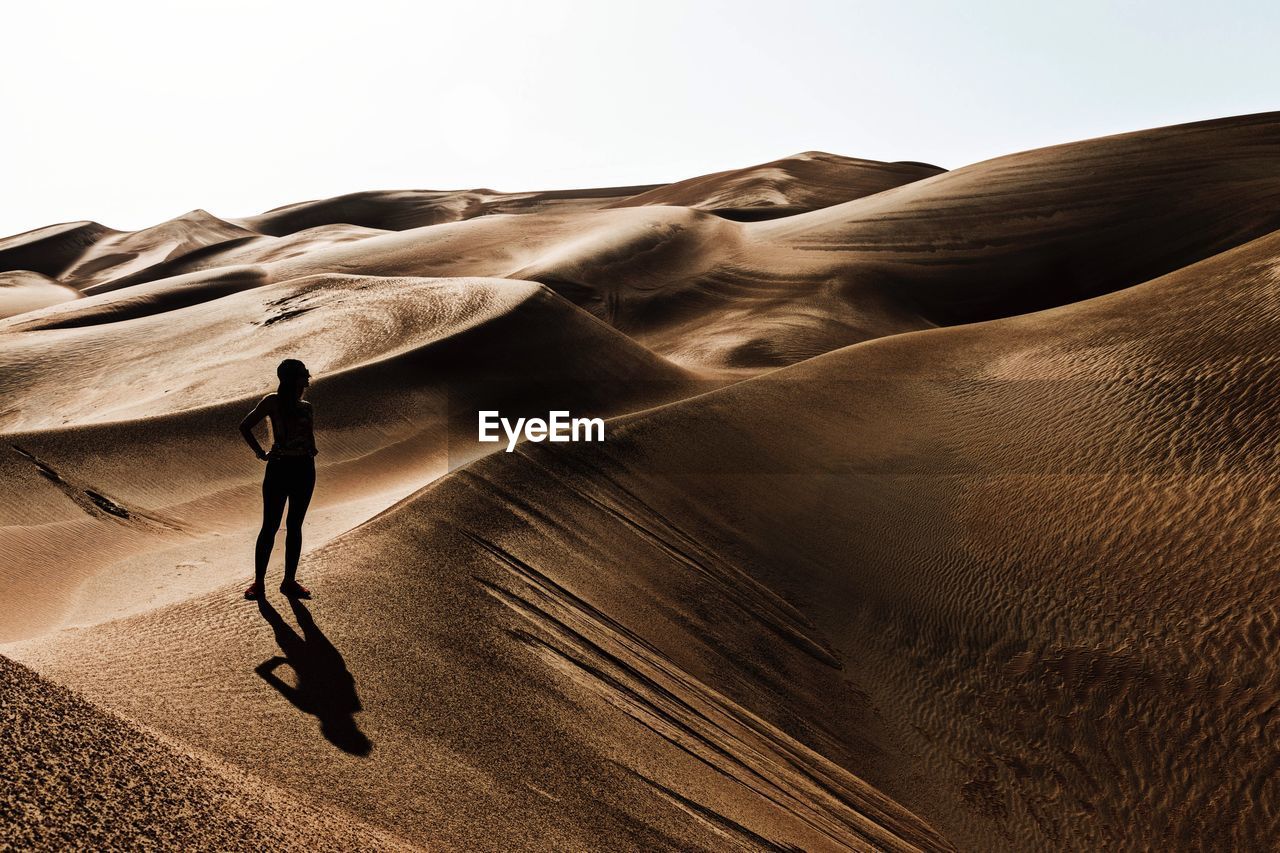 Woman standing on sand dune in desert against clear sky