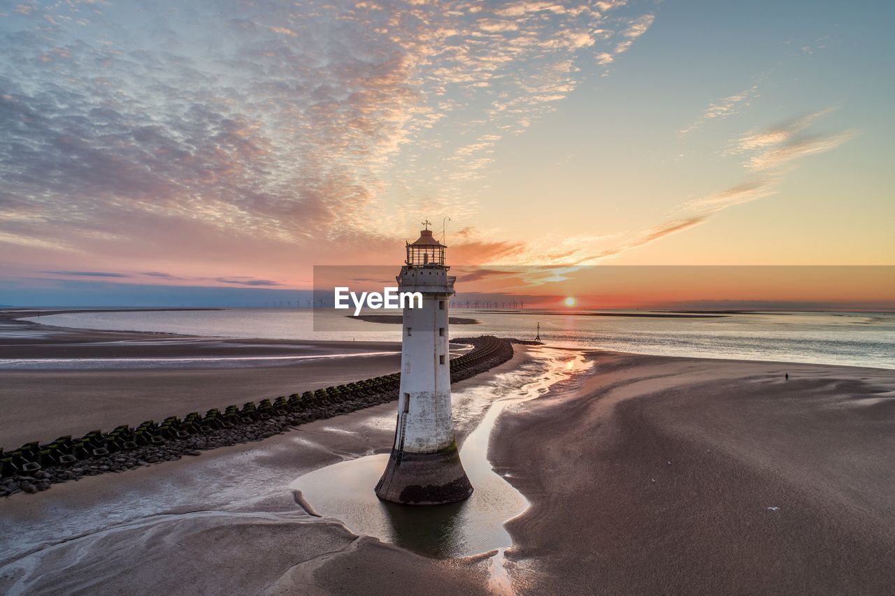 Lighthouse by sea against sky during sunset