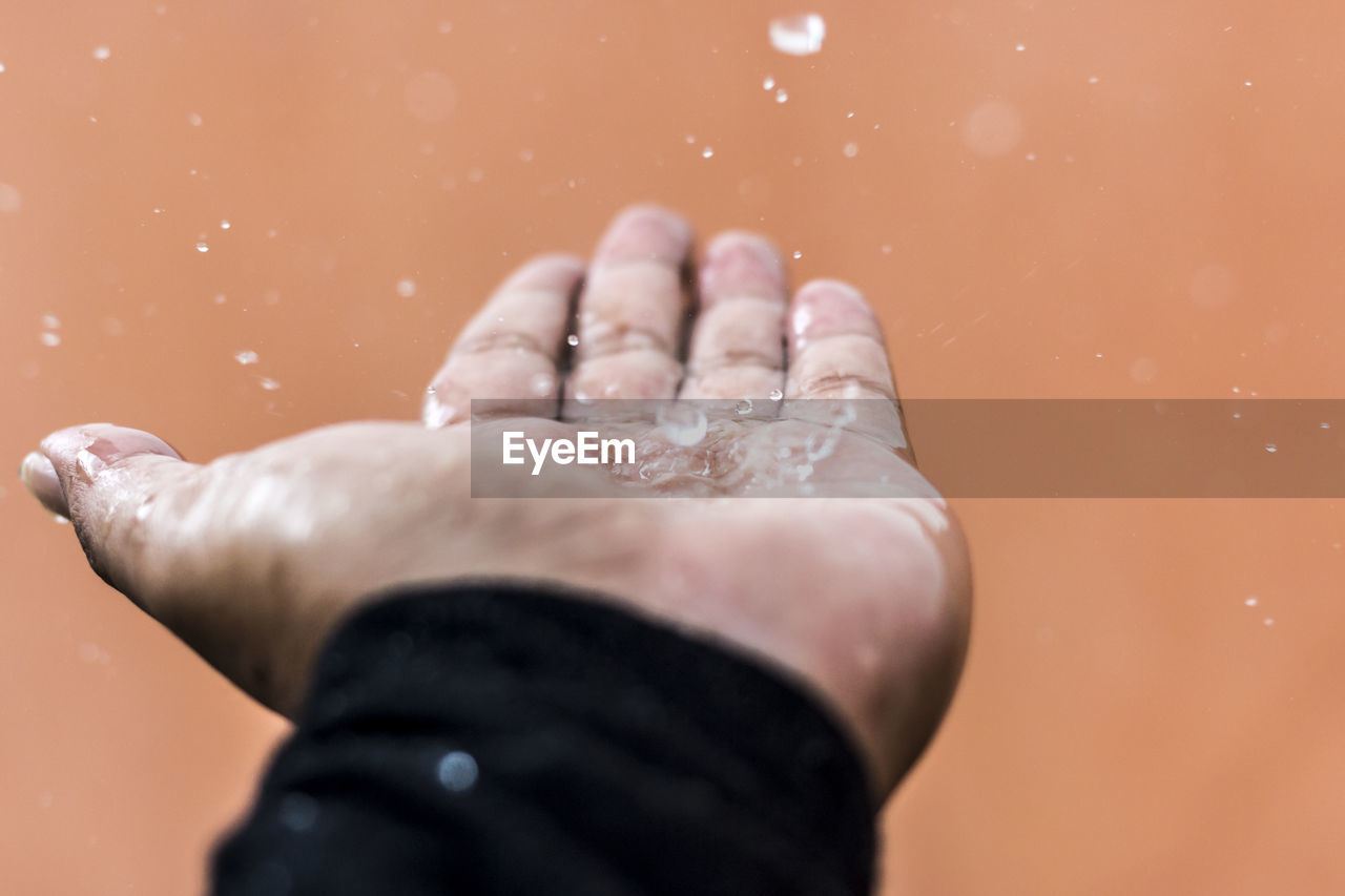 Close-up of water drops falling on hand against wall