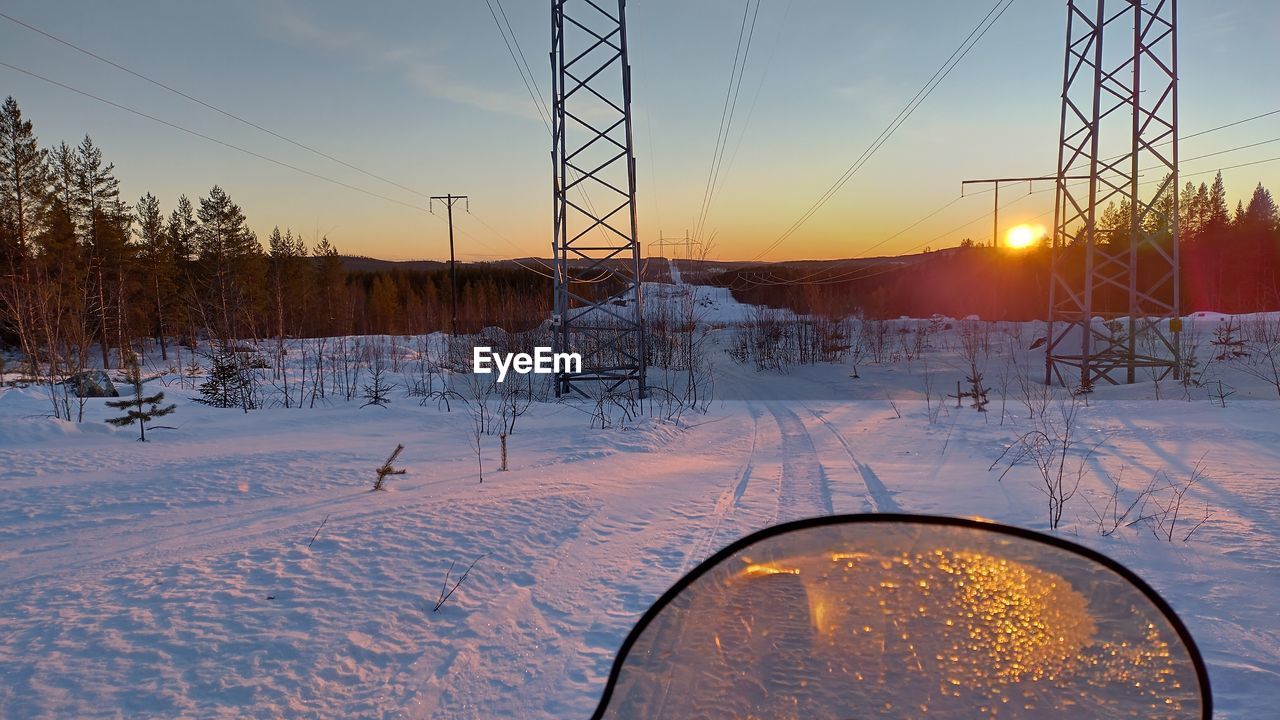 winter, snow, cold temperature, sunset, sky, nature, environment, landscape, scenics - nature, beauty in nature, frozen, tree, freezing, sunlight, sun, no people, tranquility, plant, tranquil scene, electricity pylon, cable, electricity, land, transportation, non-urban scene, outdoors, dusk, evening, rural scene, twilight, cloud, technology, power line, reflection, ice, orange color