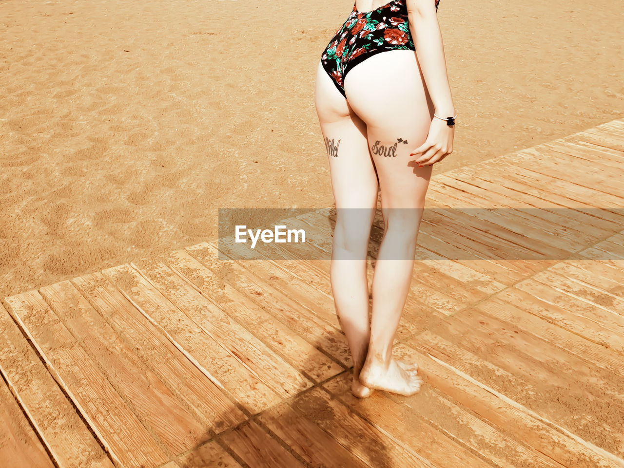 Low section of seductive woman standing on floorboard at beach during sunny day