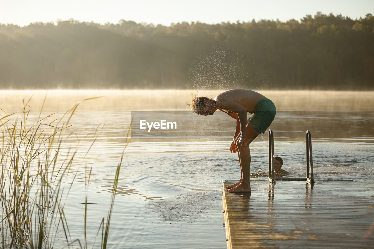 Young man shaking off water at lake