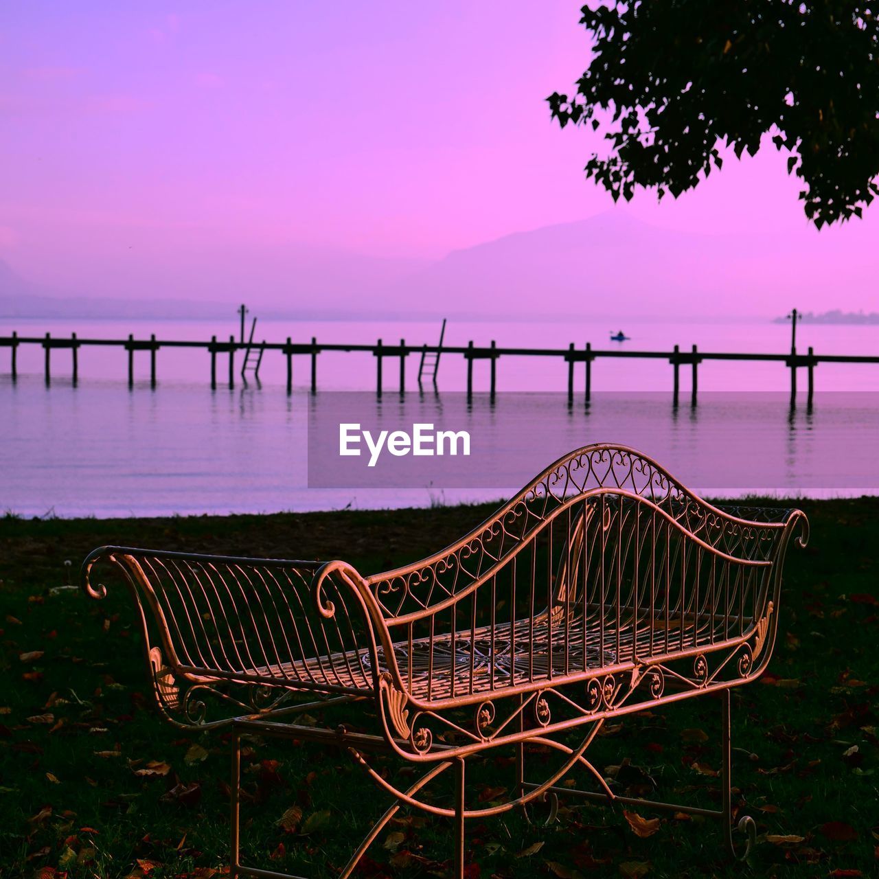 EMPTY CHAIR BY LAKE AGAINST SKY AT SUNSET