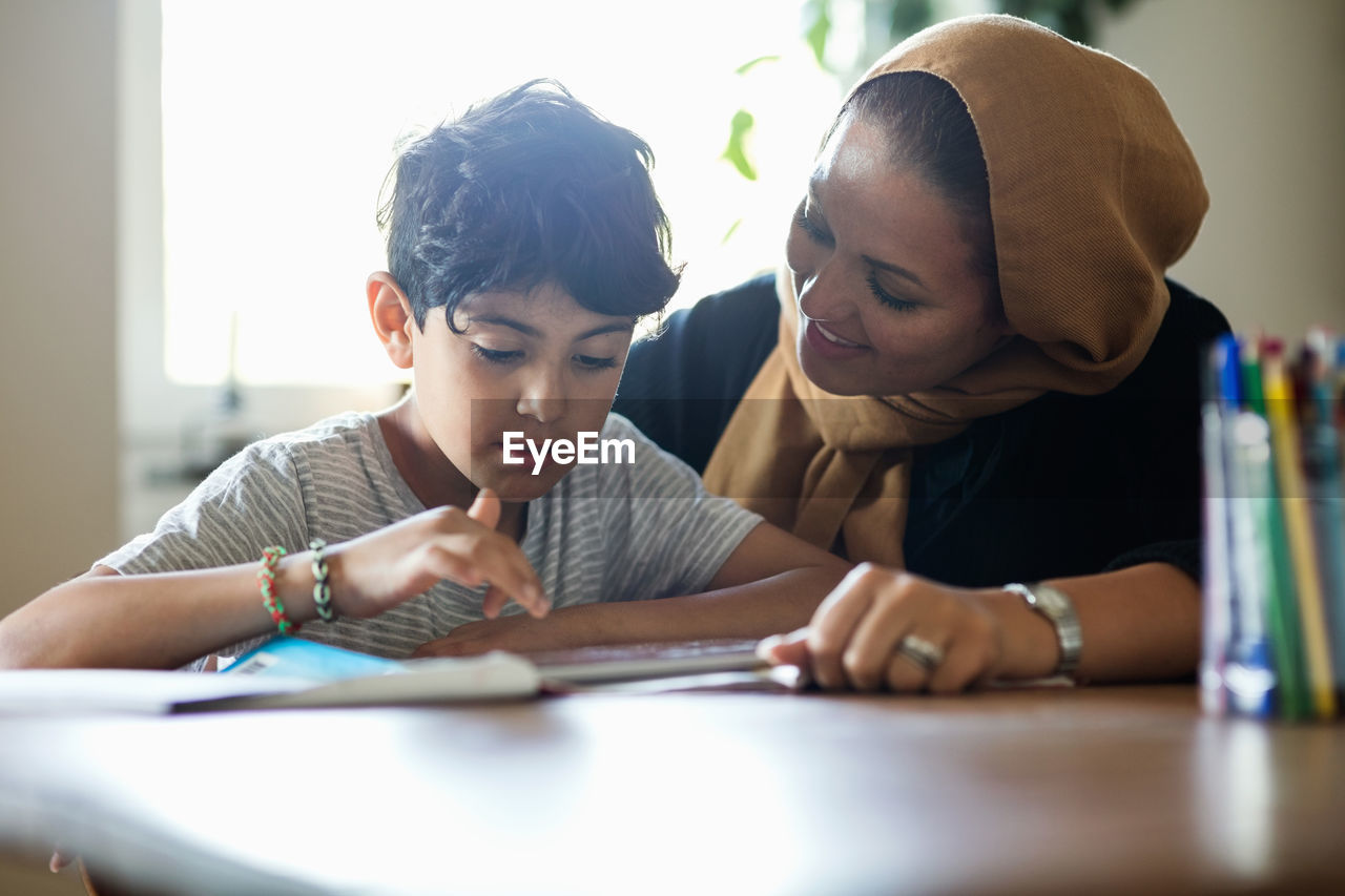 Smiling mother assisting son in using digital tablet while studying at home