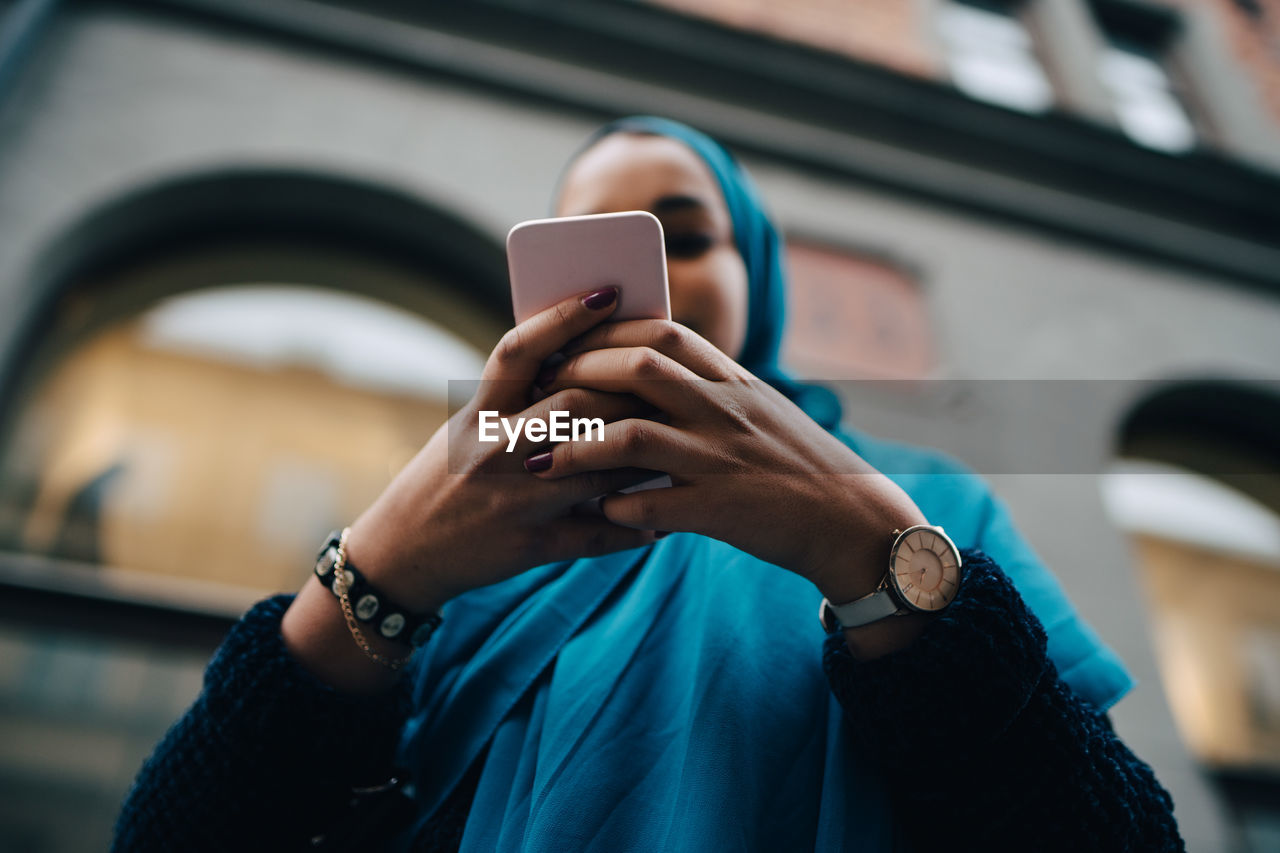 Low angle view of young woman using smart phone against building in city