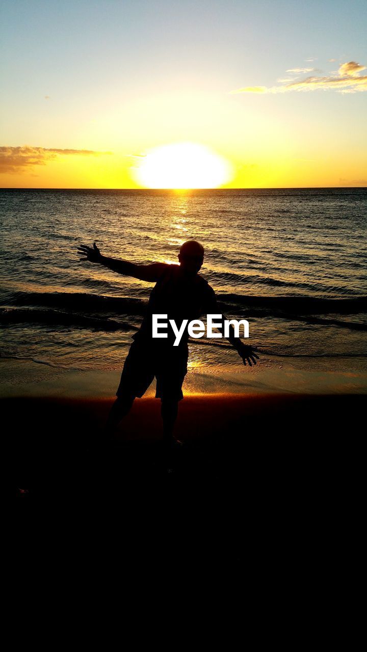 Silhouette man standing on shore against sea during sunset