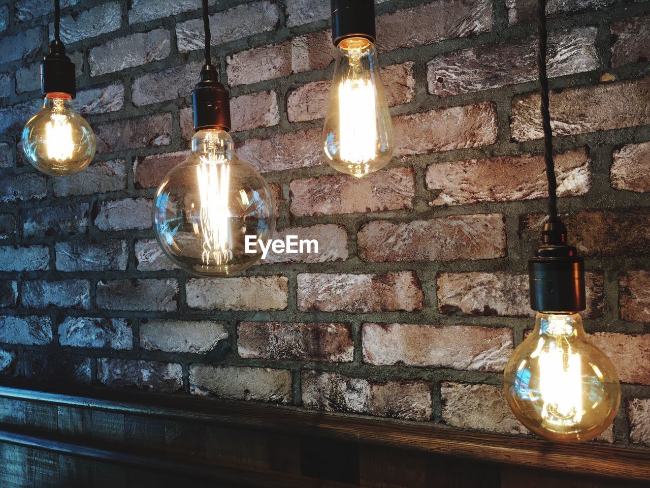 Illuminated light bulbs hanging by brick wall