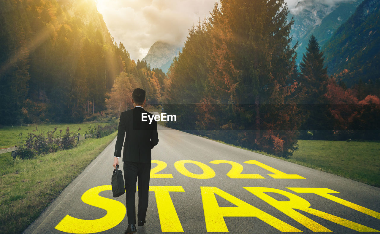 REAR VIEW OF MAN STANDING BY ROAD AGAINST SKY