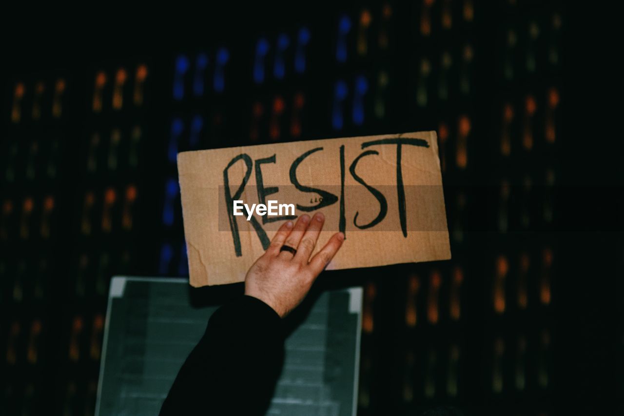 Cropped hand of person holding resist text on cardboard