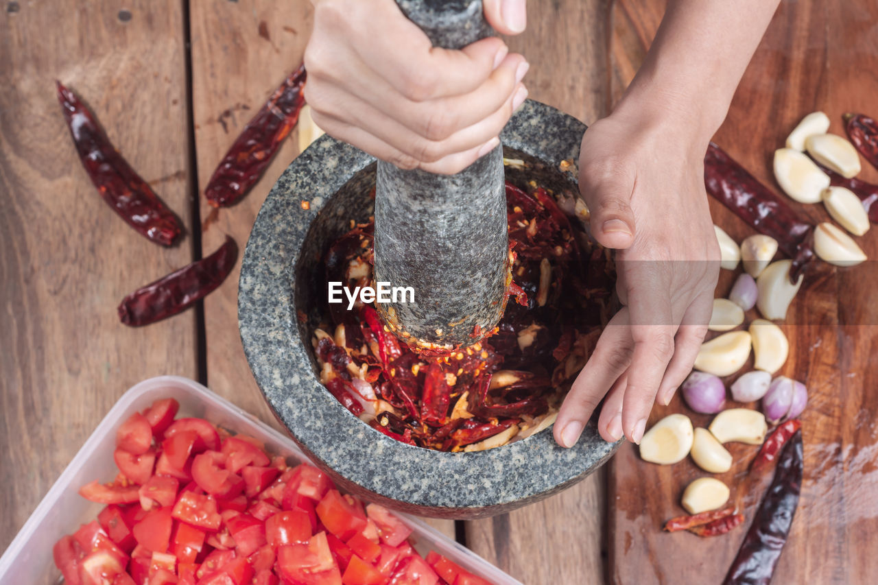 Cropped hands of woman crushing red chili pepper in mortar and pestle