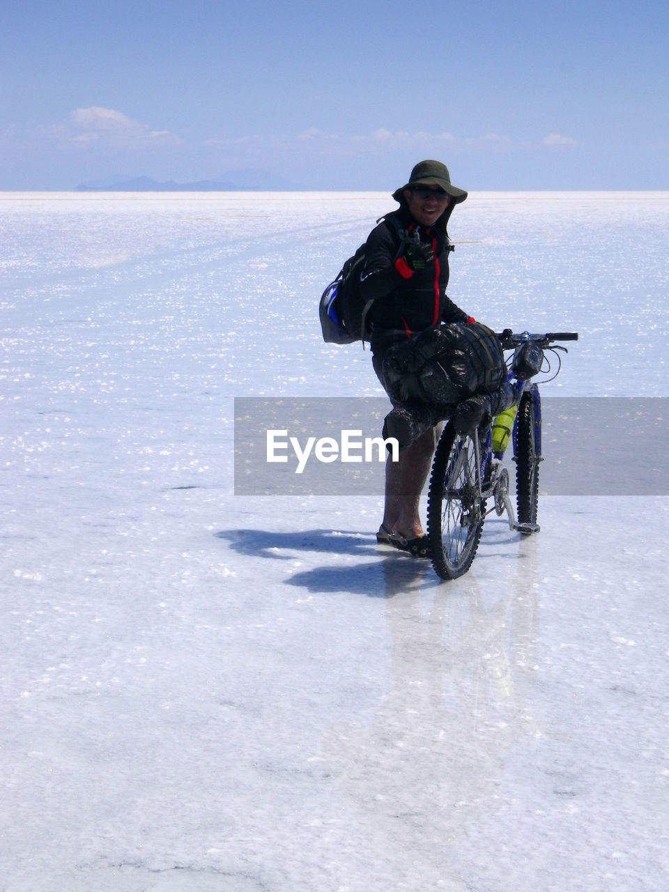 Portrait of mid adult man with bicycle standing at salar de uyuni against blue sky