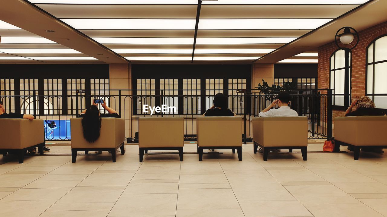 REAR VIEW OF PEOPLE SITTING IN ILLUMINATED ROOM