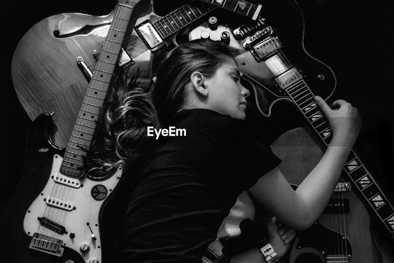 Young woman sleeping amidst guitar on black background