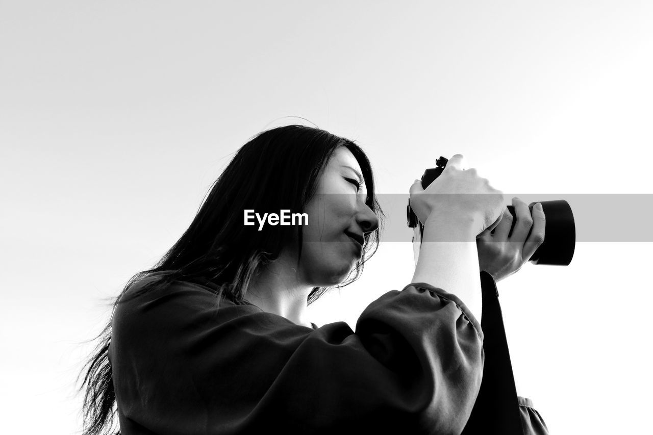 Low angle view of woman photographing against sky