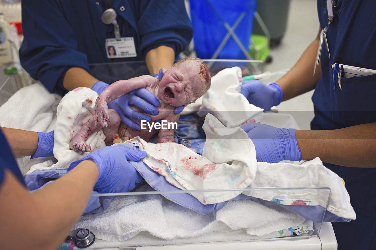 Midsection of doctors holding newborn baby boy in crib at hospital