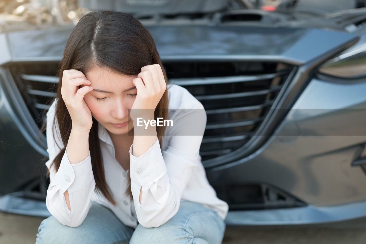 Stressed woman crouching against car