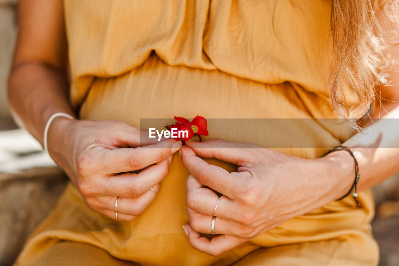 Midsection of pregnant woman holding flower while sitting outdoors