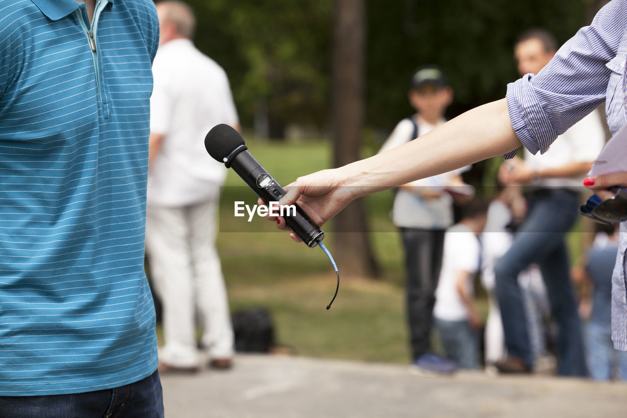 Cropped hand of woman holding microphone in front of man