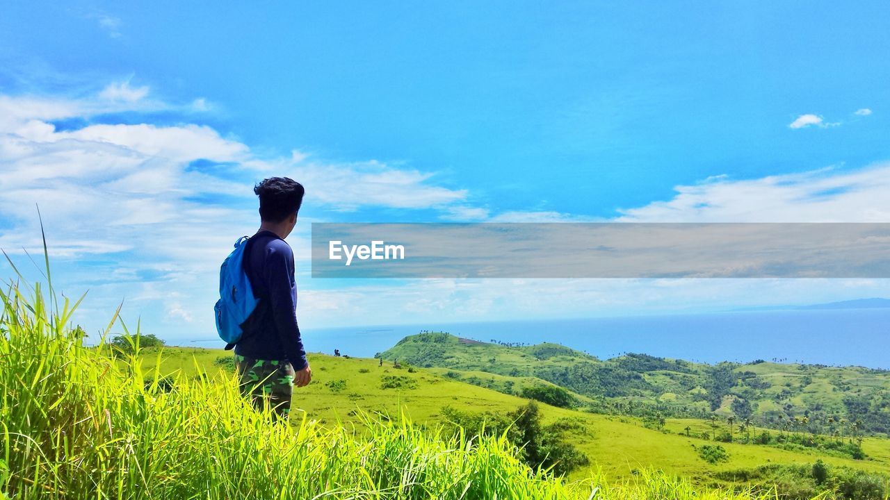 Side view of man standing on field against sky