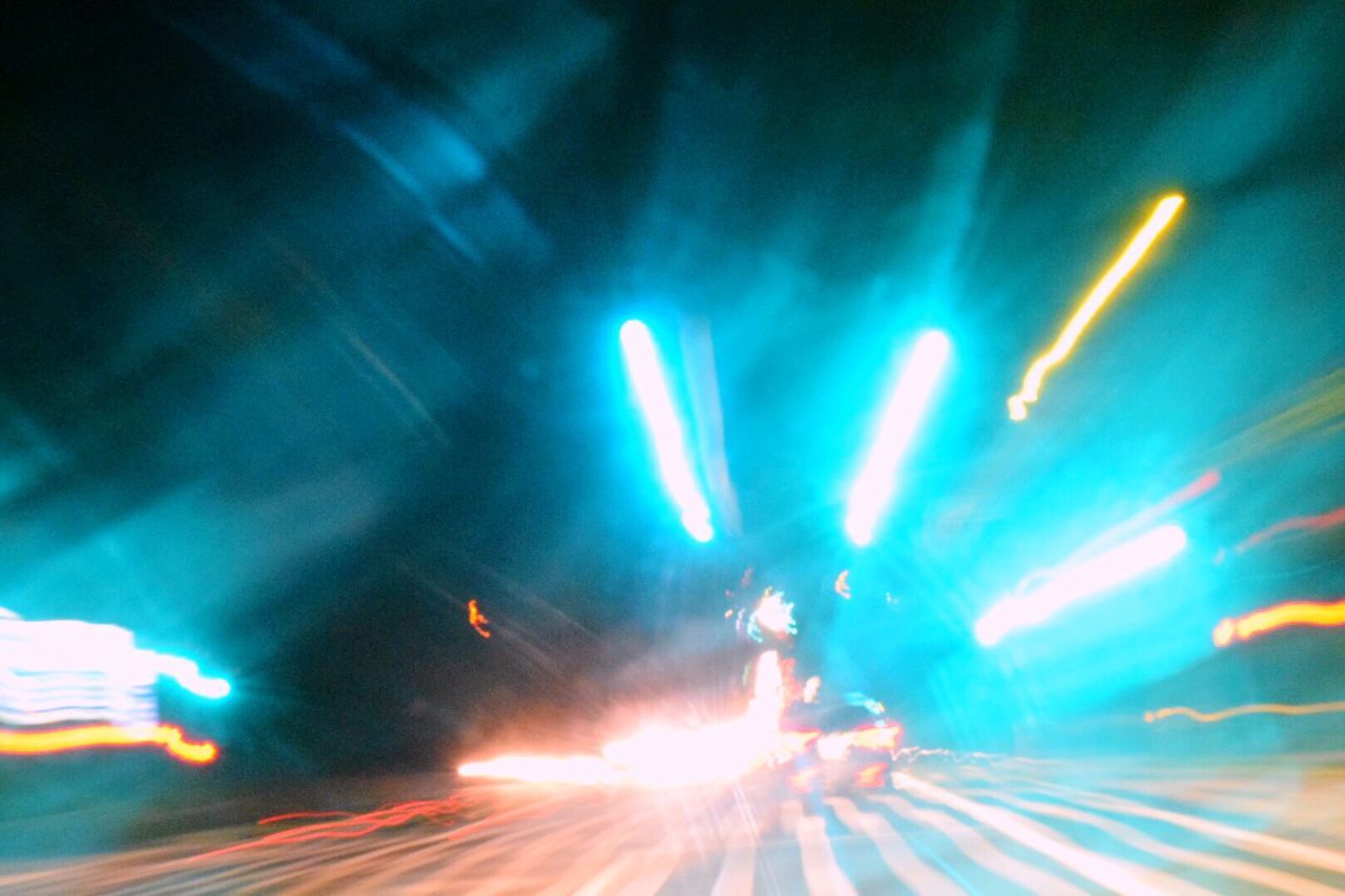 LIGHT TRAILS ON ROAD AGAINST BRIGHT LIGHTS AT NIGHT