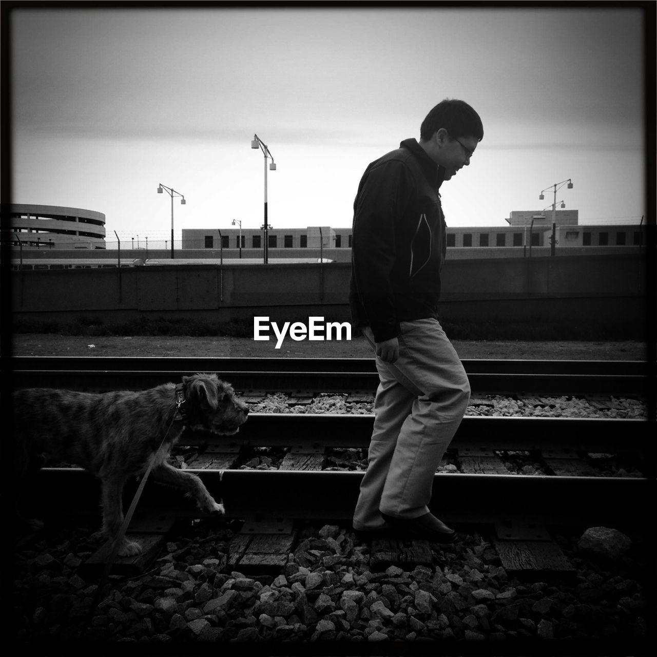 Full length of man with dog walking on railroad track against sky