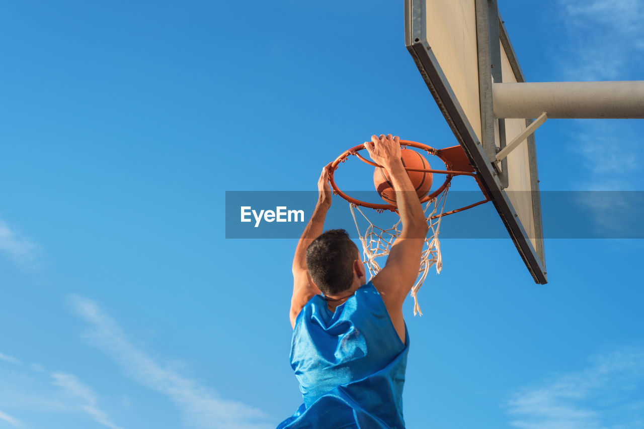 Low angle view of man playing basketball against blue sky