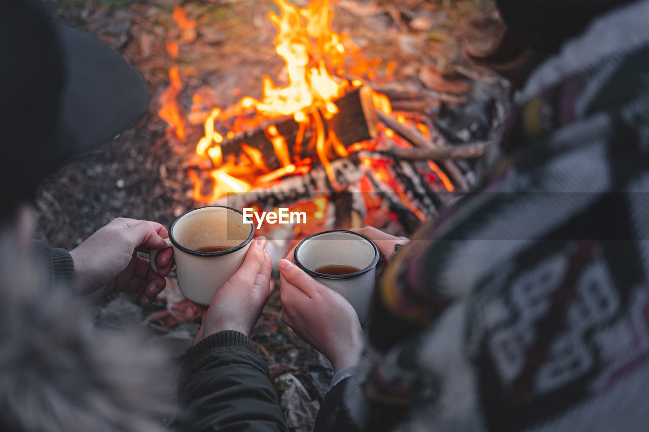 High angle view of couple having coffee in cups against campfire