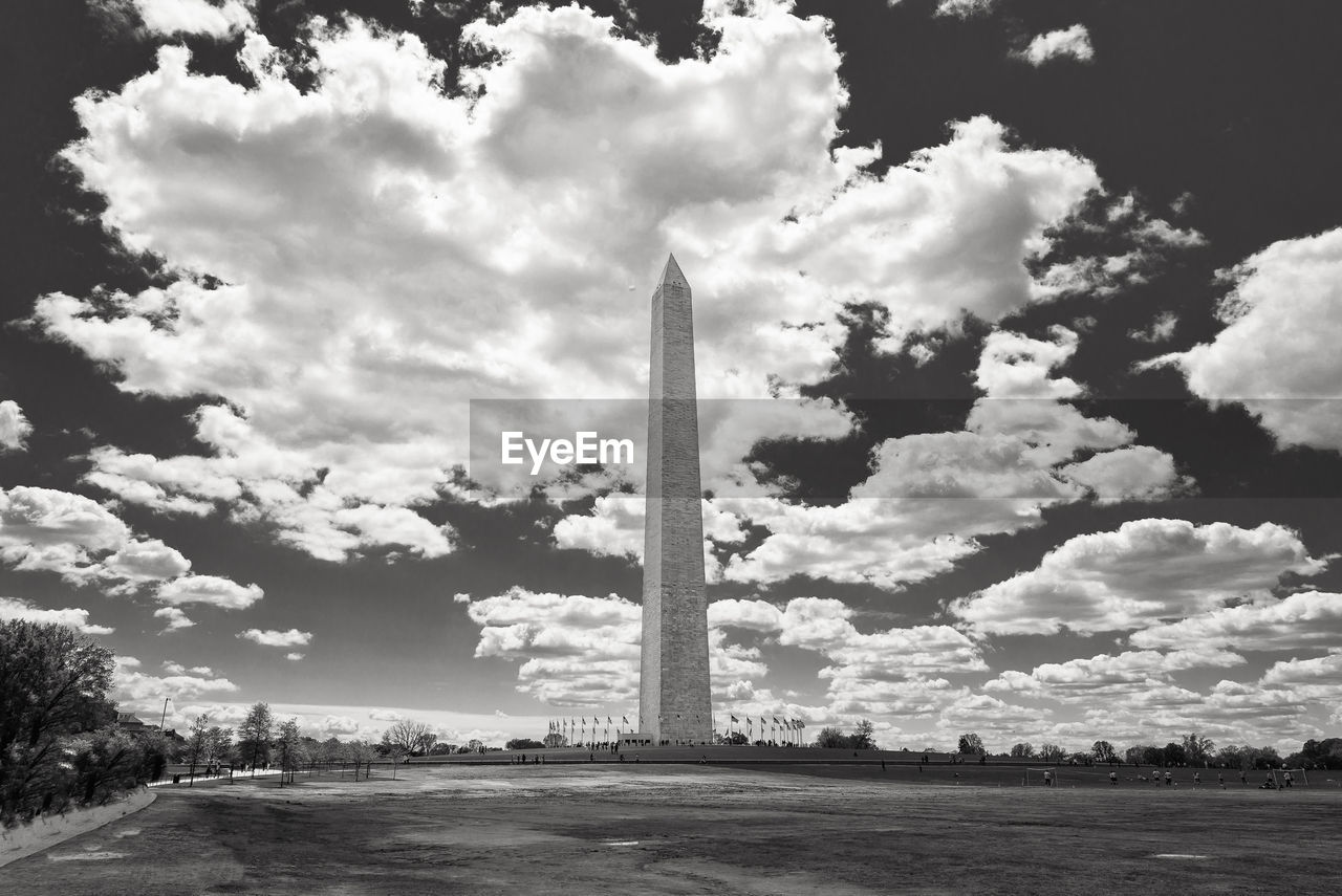 Washington monument on field against cloudy sky