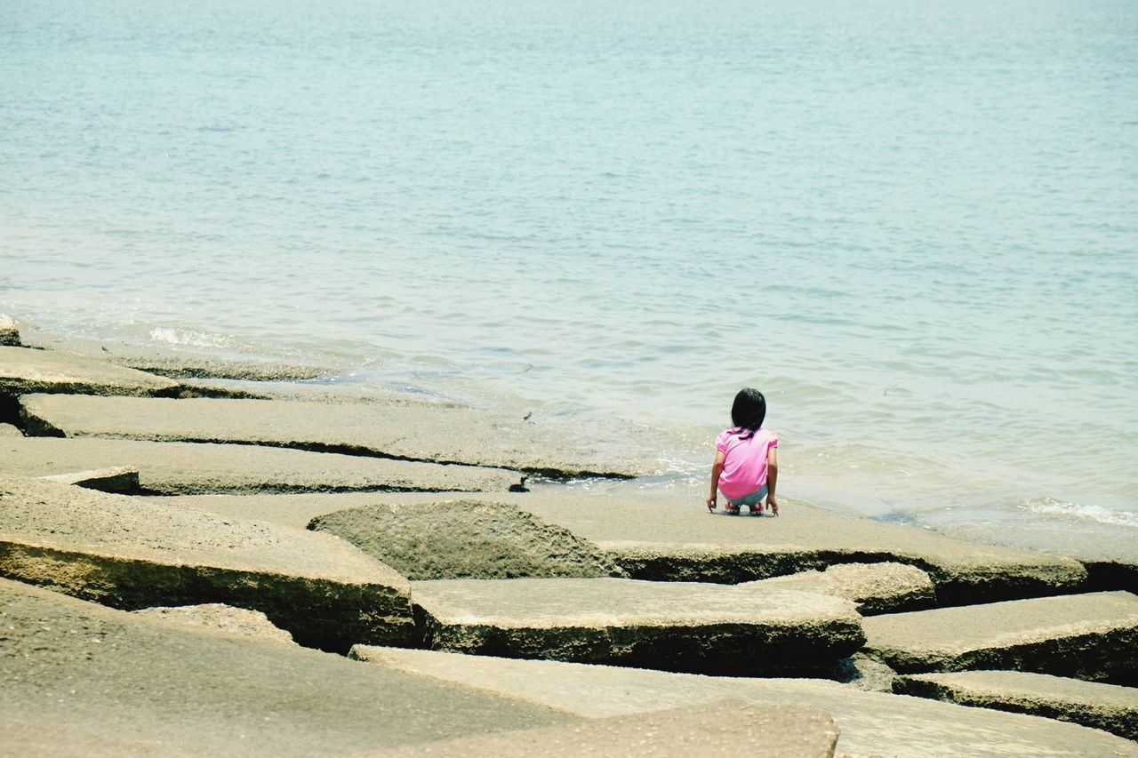 Rear view of girl crouching at beach