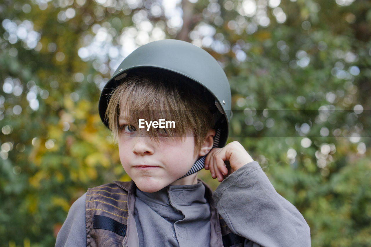 A boy dressed in a soldier costume tugs at the strap of his helmet