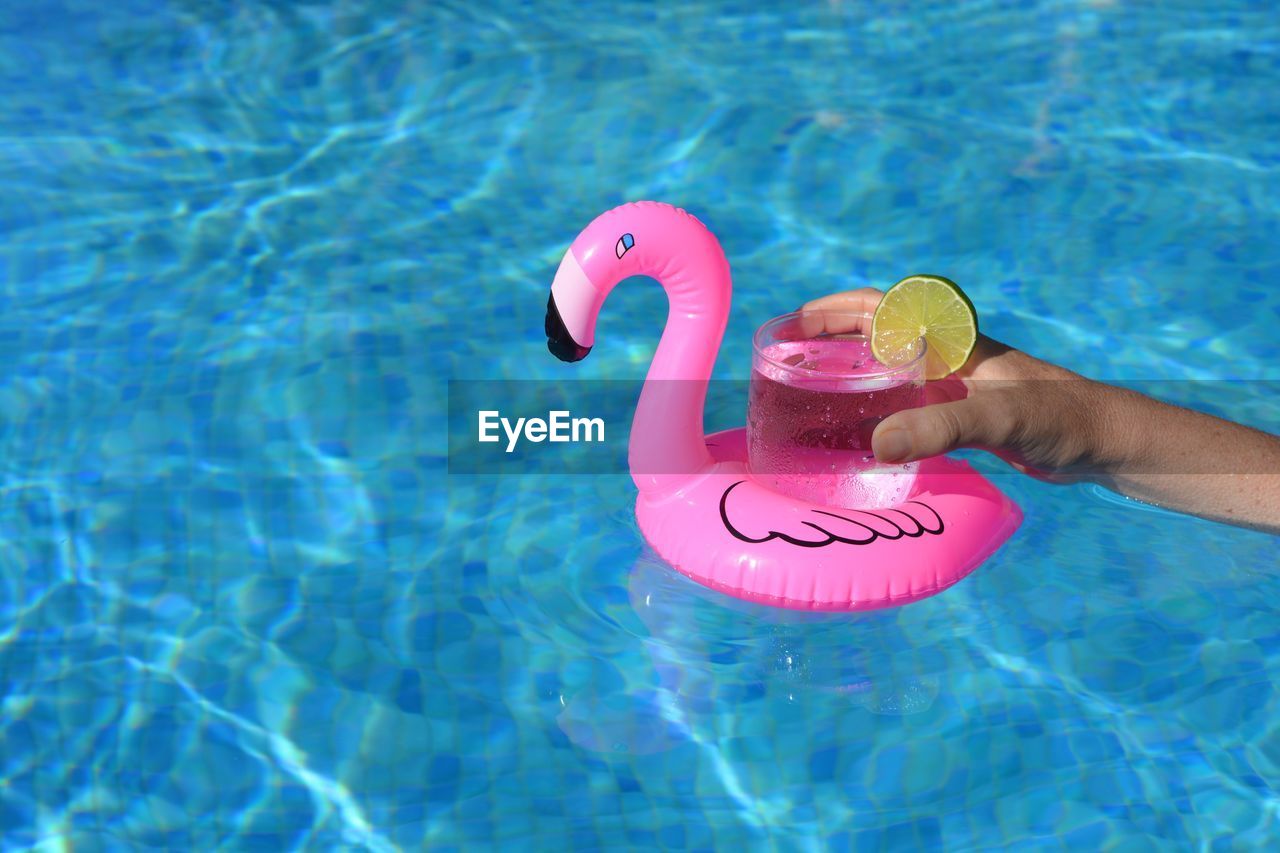 Cropped hand holding drink on inflatable ring in swimming pool