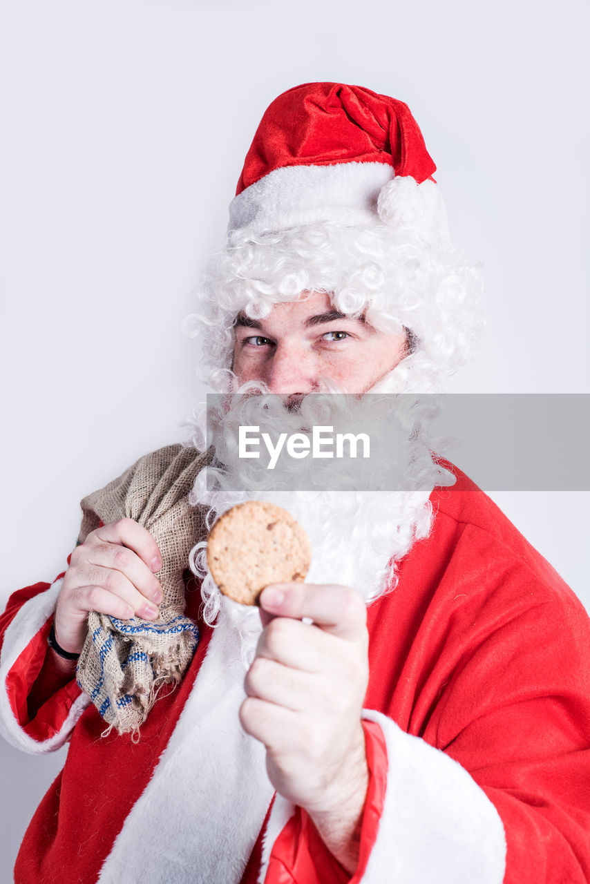 Portrait of man in santa costume giving cookie against white background