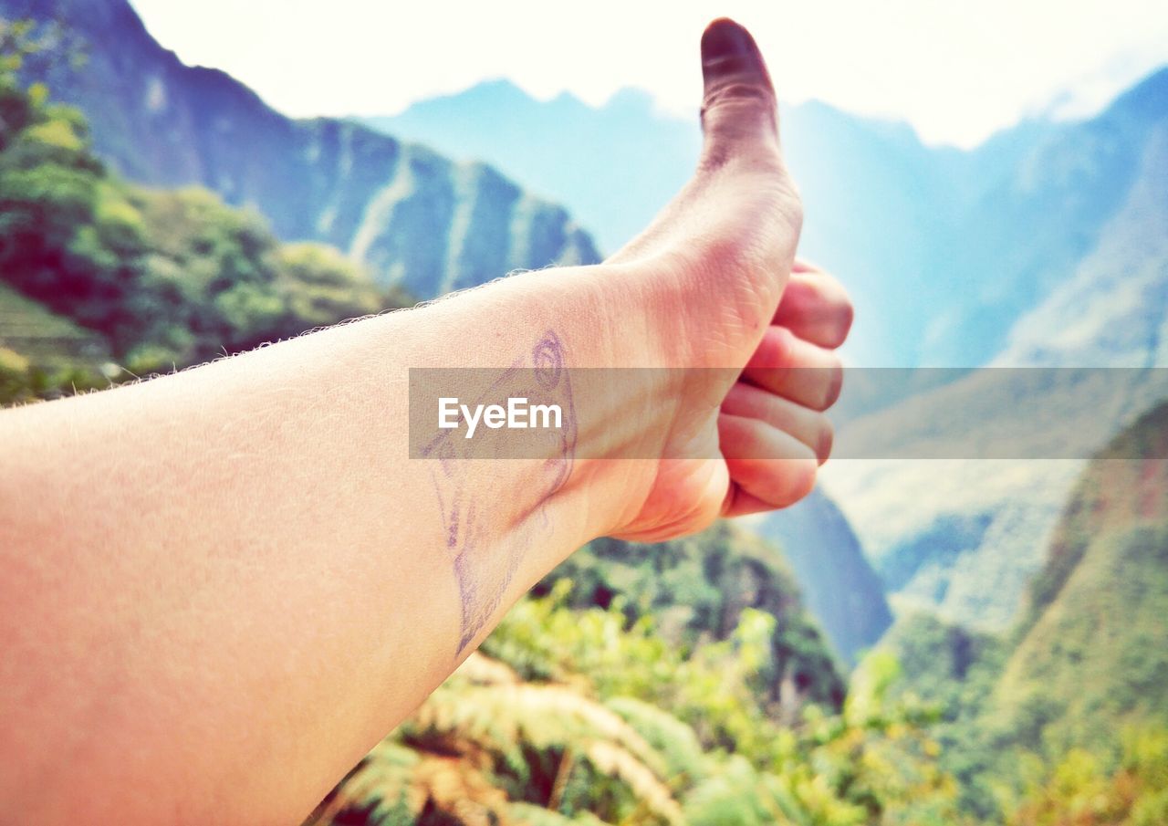 CLOSE-UP OF WOMAN HAND AGAINST MOUNTAINS