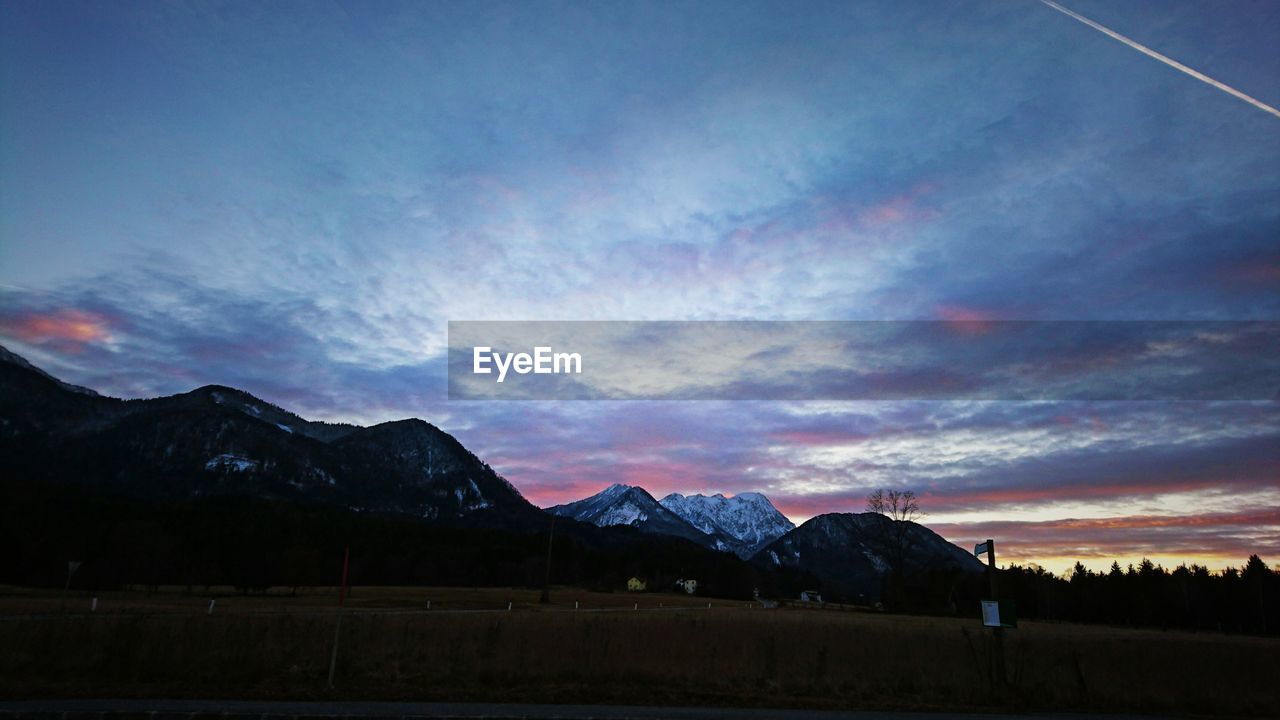 SCENIC VIEW OF MOUNTAINS AGAINST CLOUDY SKY AT SUNSET