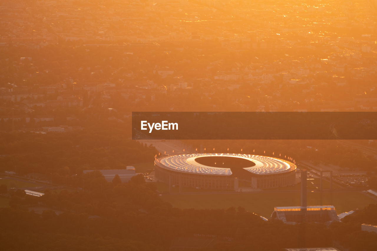 High angle view of illuminated ferris wheel against orange sky