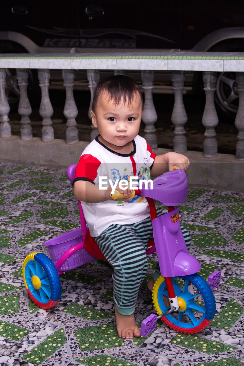 PORTRAIT OF CUTE GIRL HOLDING TOY WHILE SITTING ON FLOOR