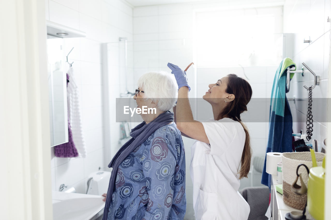 Nurse combing woman's hair in bathroom