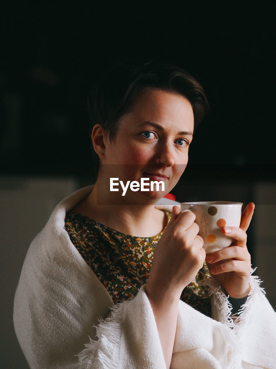Portrait of a young woman with short hair at home with a cup of coffee or tea in the evening.