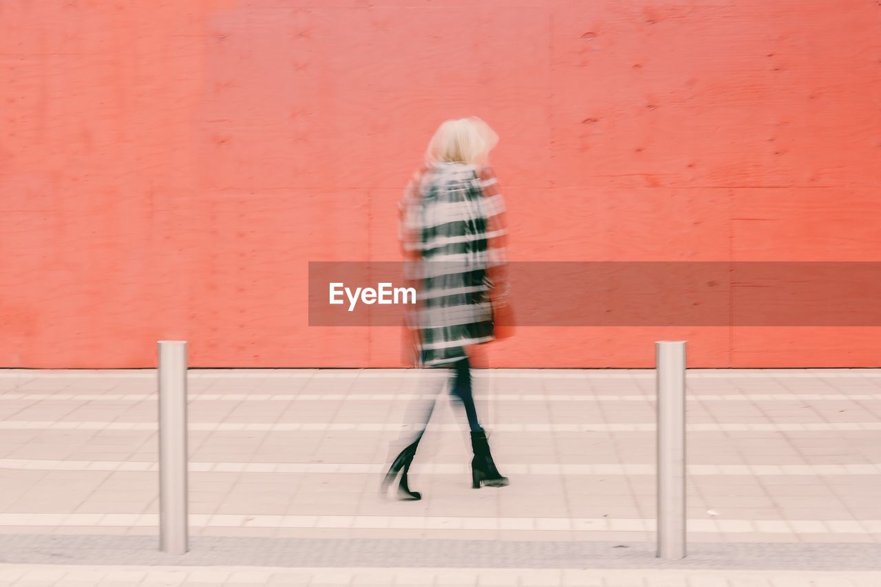 Woman walking on footpath against wall