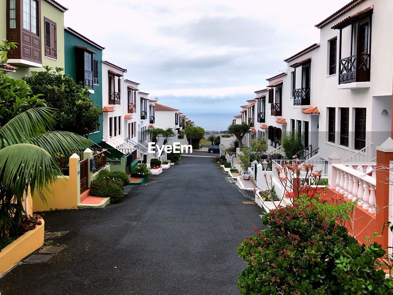 Empty road amidst buildings against cloudy sky