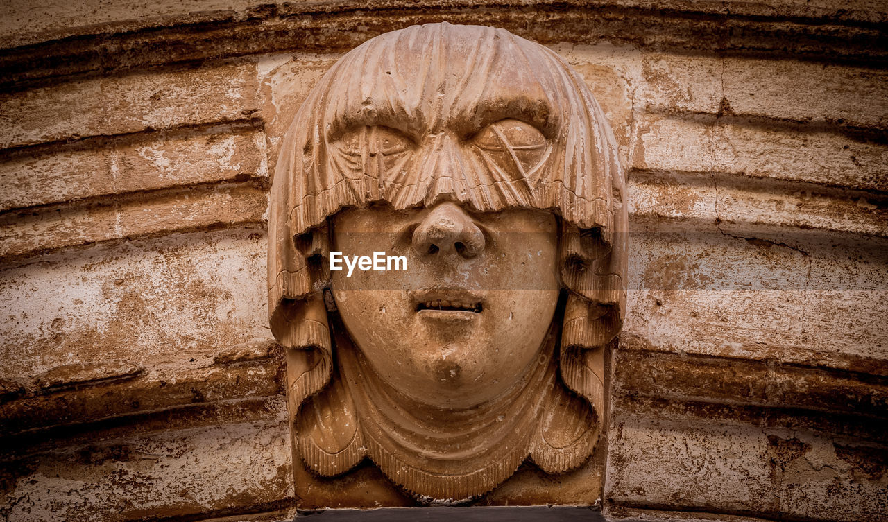 CLOSE-UP OF OLD STATUE AGAINST BRICK WALL