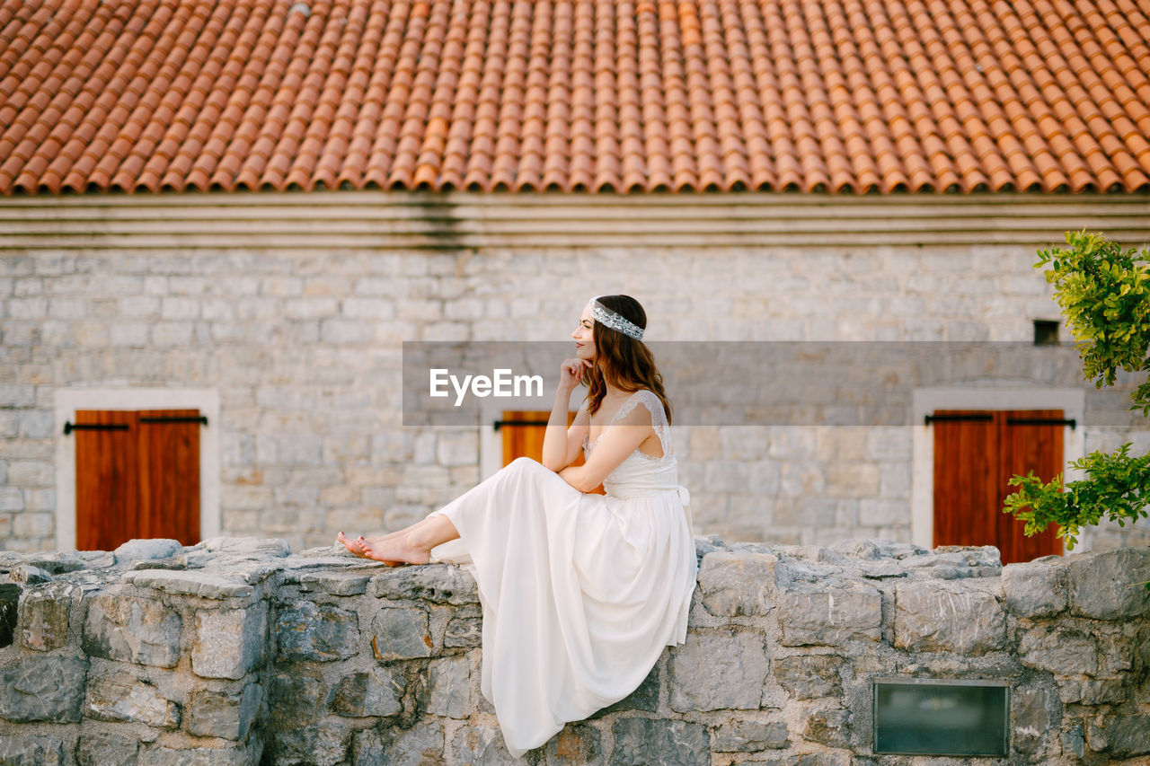 Side view of bride siting against house