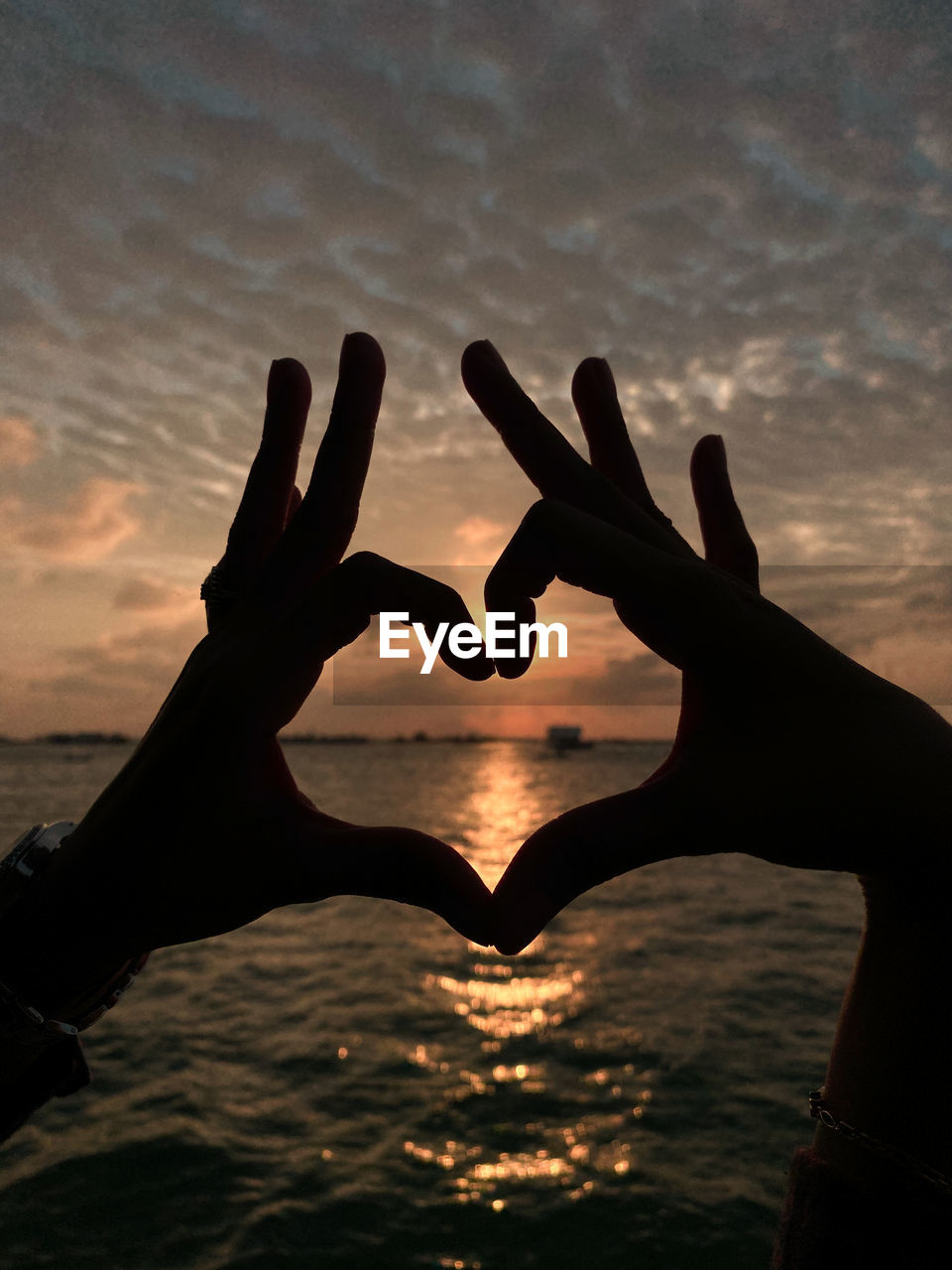 Silhouette hand making heart shape over sea against sky during sunset