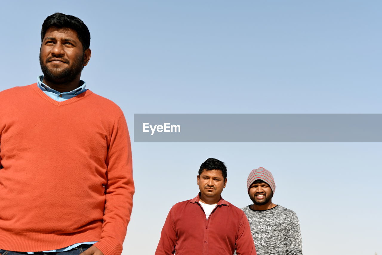 Smiling men standing against sky