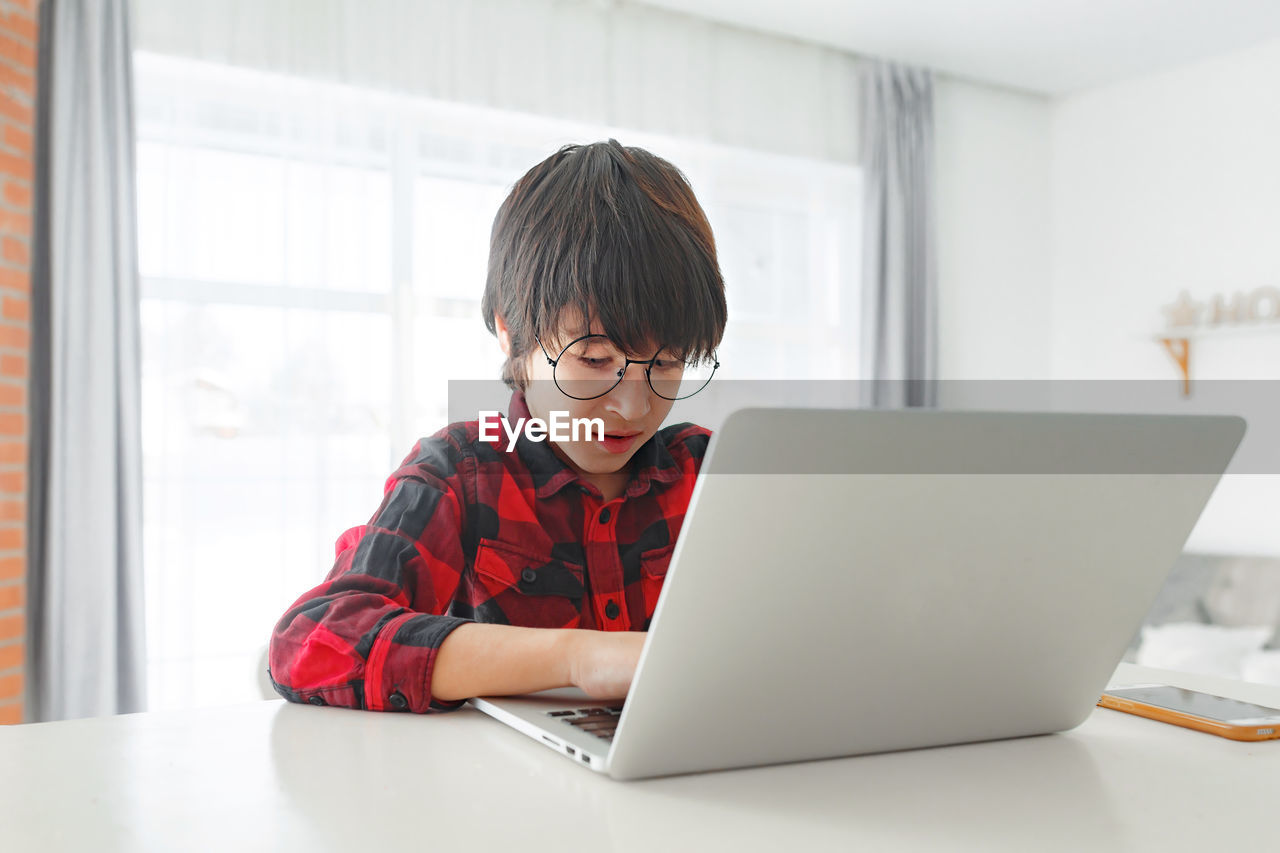 Young boy in eyeglasses using laptop at home